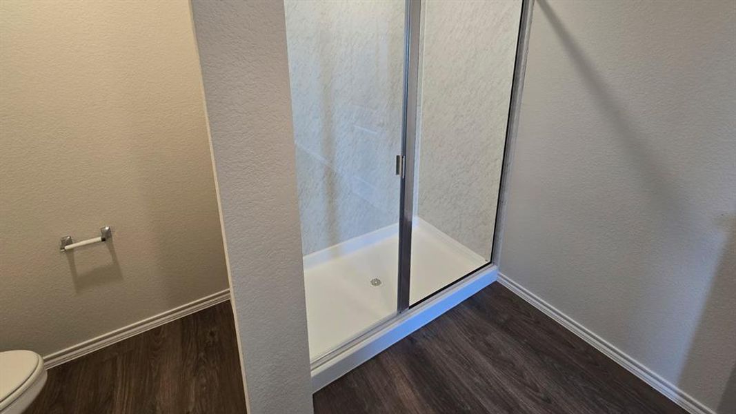 Bathroom with a textured wall, dark wood finished floors, and a shower stall Bathroom with a textured wall, dark wood finished floors, and a shower stall