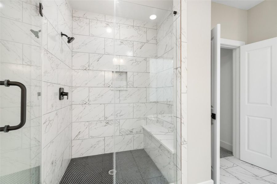 The spacious, modern shower is a true standout, featuring sleek glass doors and elegant white marble tiles. With dual shower heads, a built-in bench, and recessed shelving for added convenience, this shower offers both luxury and functionality, creating a perfect space for relaxation.