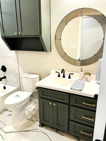 Bathroom featuring a dark green vanity with brass hardware, a white undermount sink, and a white countertop Bathroom featuring a dark green vanity with brass hardware, a white undermount sink, and a white countertop