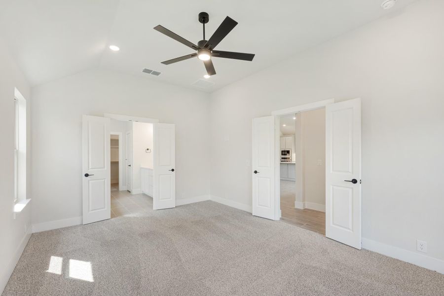 Empty master bedroom with carpet, black ceiling fan, and open doors to walk-in closet and bathroom