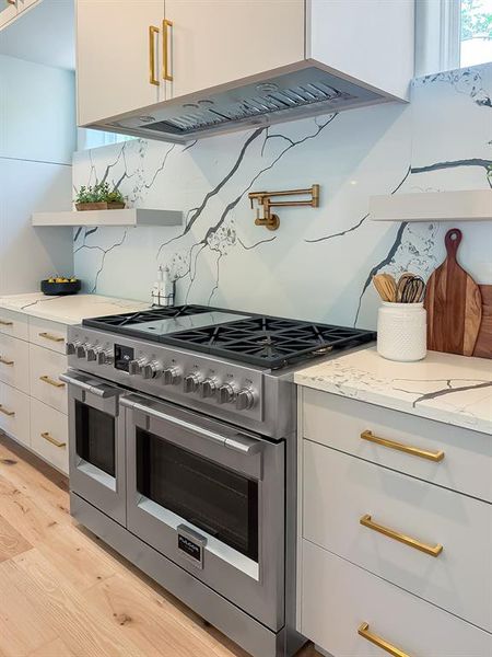 Kitchen with under cabinet range hood, double oven range, white cabinetry, light stone countertops, and light wood-style floors Kitchen with under cabinet range hood, double oven range, white cabinetry, light stone countertops, and light wood-style floors