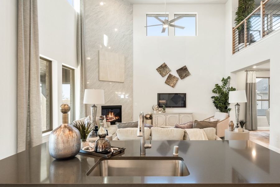 Open-concept living room with two-story ceilings, marble fireplace, and kitchen island in foreground