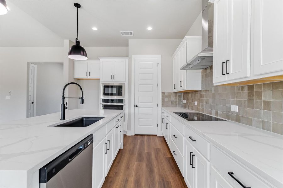 Kitchen featuring light stone counters, stainless steel appliances, dark wood-style floors, an island with sink, and white cabinetry
