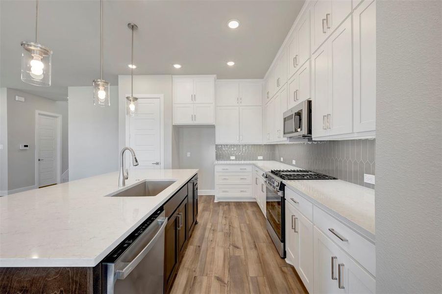 Kitchen featuring stainless steel appliances, an island with sink, dual tone cabinetry, light stone counters, and light wood-style floors