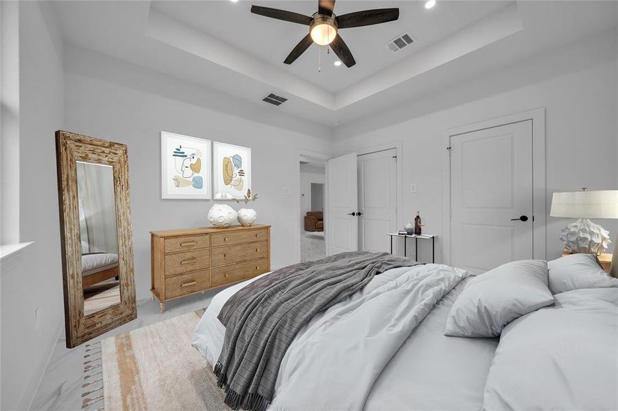Bedroom with ceiling fan, a raised ceiling, and multiple closets