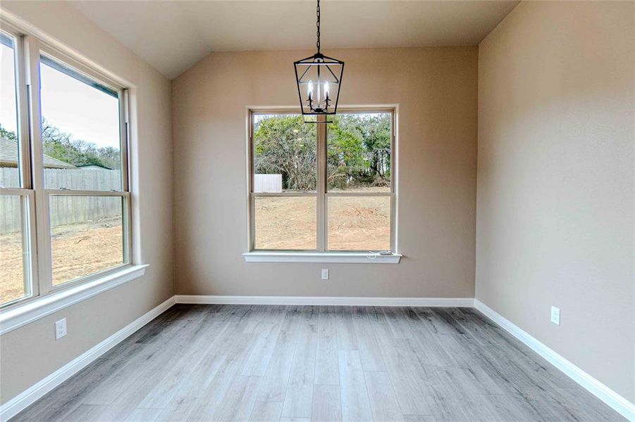 Unfurnished dining area with lofted ceiling, an inviting chandelier, and light hardwood / wood-style flooring