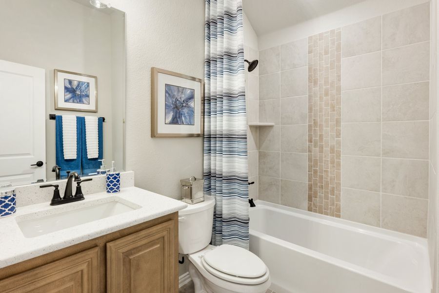 Bathroom with wood vanity, white countertop, toilet, and tiled tub-shower combo with striped curtain