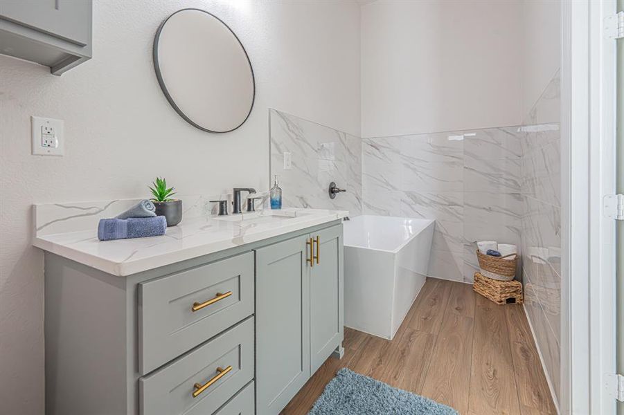 Full bathroom featuring a soaking tub, vanity, light wood-style flooring, a marble finish shower, and tile walls Full bathroom featuring a soaking tub, vanity, light wood-style flooring, a marble finish shower, and tile walls