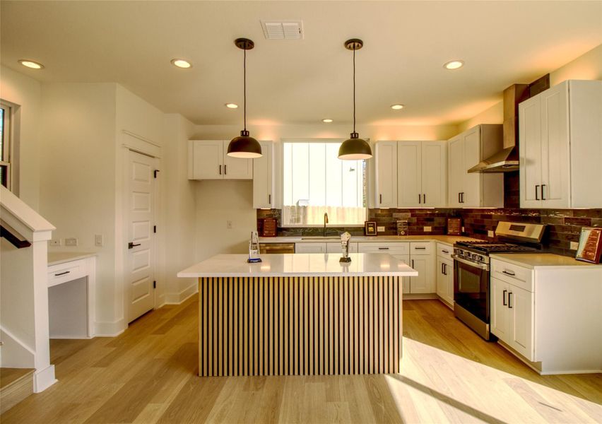 Kitchen with gas stove, light wood-style flooring, wall chimney exhaust hood, pendant lighting, and recessed lighting