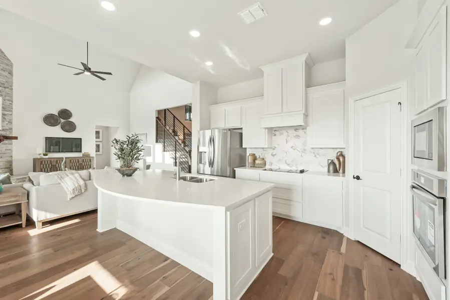 Open-concept kitchen with white cabinets, large island, stainless steel appliances, and hardwood floors open to living area.