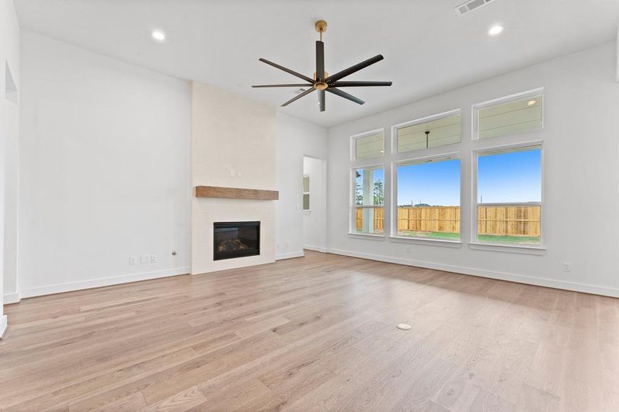 Family Room Featuring Gas Log Fireplace with Tile Surround to the Ceiling, Engineered Hardwood Flooring, Fan, and Floor Outlet.