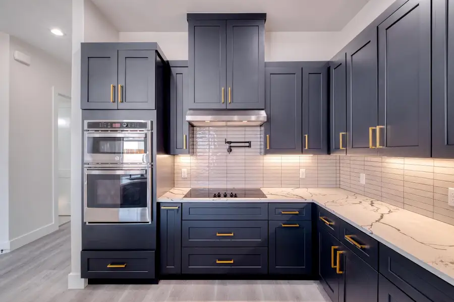 Kitchen featuring under cabinet range hood, light stone counters, tasteful backsplash, double oven, and black electric cooktop