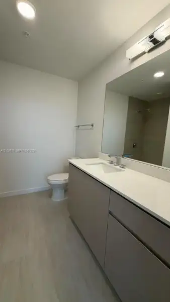 Bathroom featuring a vanity with a white countertop and rectangular undermount sink, flat-panel cabinetry, large wall-mounted mirror, overhead light fixture, and tile flooring