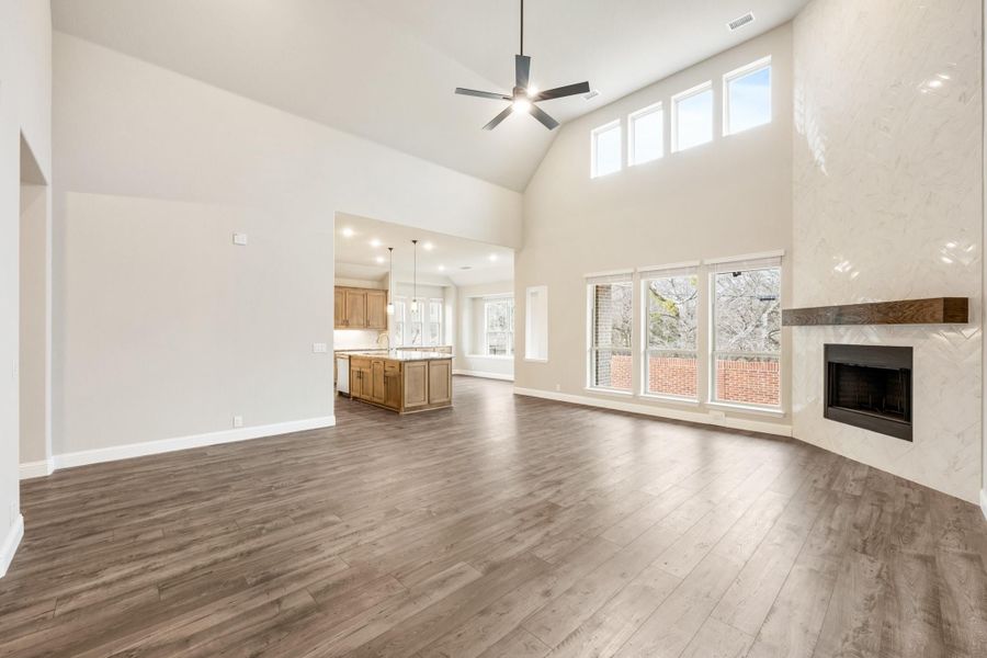 Open living room with vaulted ceiling, hardwood floors, stone fireplace, and open kitchen beyond Open living room with vaulted ceiling, hardwood floors, stone fireplace, and open kitchen beyond