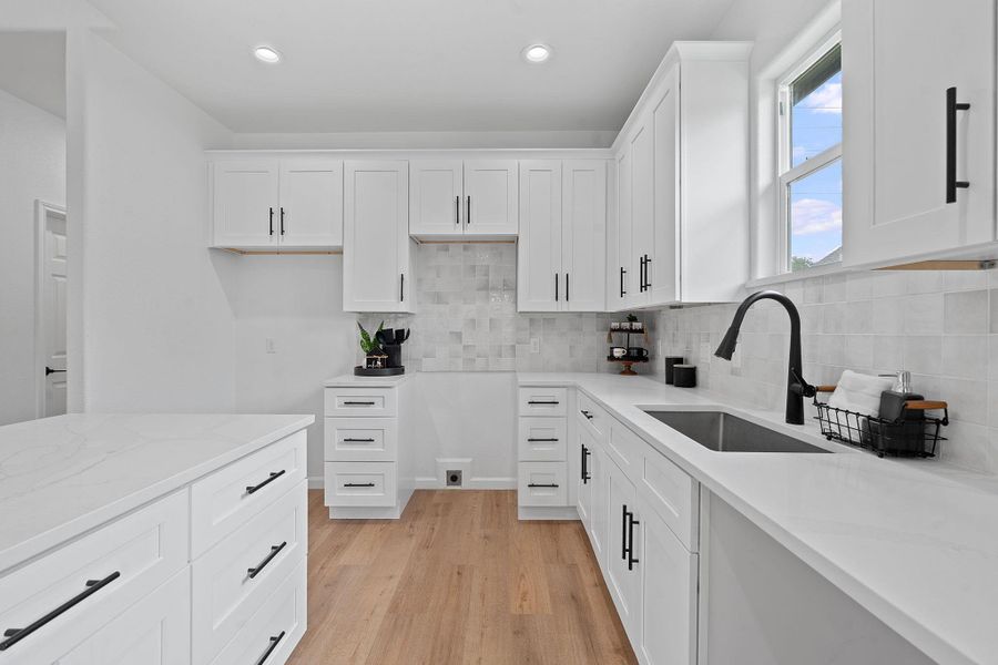 Kitchen with white cabinets, light wood-type flooring, light stone countertops, backsplash, and recessed lighting