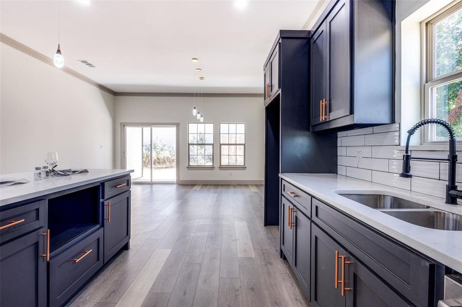 Kitchen featuring pendant lighting, crown molding, sink, decorative backsplash, and plenty of natural light