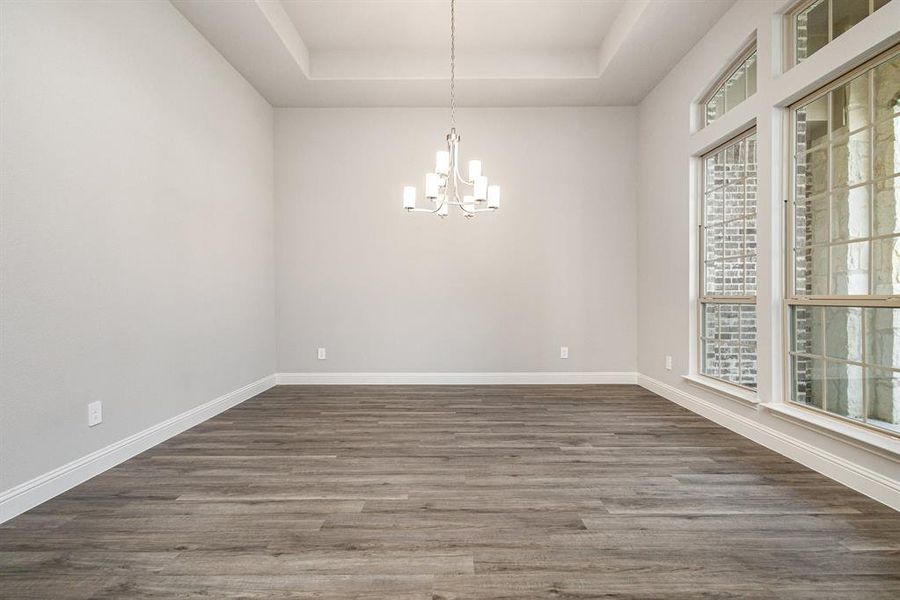 Empty room featuring a raised ceiling, dark wood-style floors, and a chandelier Empty room featuring a raised ceiling, dark wood-style floors, and a chandelier