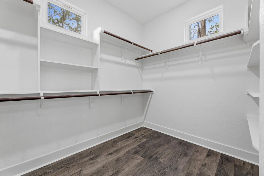 An organized closet featuring ample shelving, hanging space, and wood-look flooring.