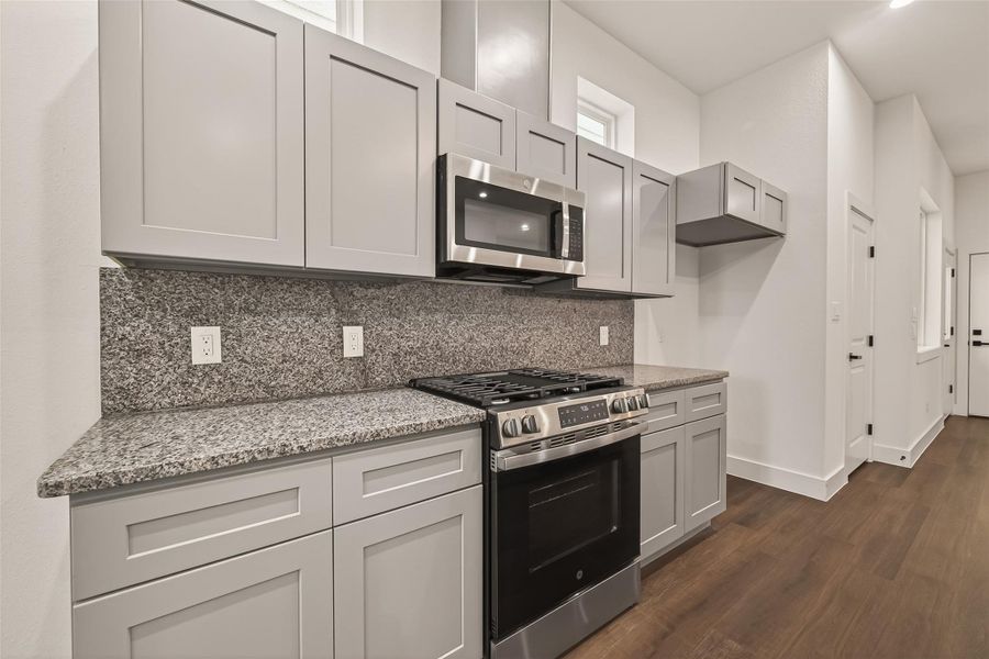 This kitchen features modern gray cabinetry, granite countertops, and stainless steel appliances, including a built-in microwave and gas range. The space is well-lit with natural light and has a sleek, contemporary design. This kitchen features modern gray cabinetry, granite countertops, and stainless steel appliances, including a built-in microwave and gas range. The space is well-lit with natural light and has a sleek, contemporary design.