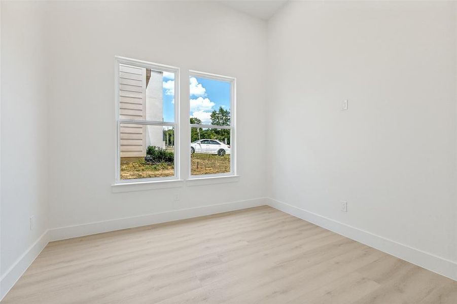 Room featuring light wood-finish flooring, white painted walls, and white baseboards Room featuring light wood-finish flooring, white painted walls, and white baseboards