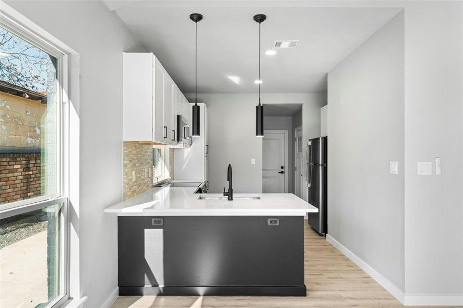 Kitchen featuring white cabinets, pendant lighting, freestanding refrigerator, light wood finished floors, and a peninsula