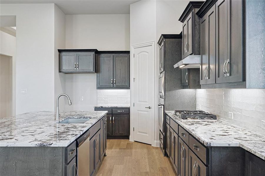 Kitchen with an island with sink, light wood-style flooring, light stone counters, stainless steel appliances, and backsplash
