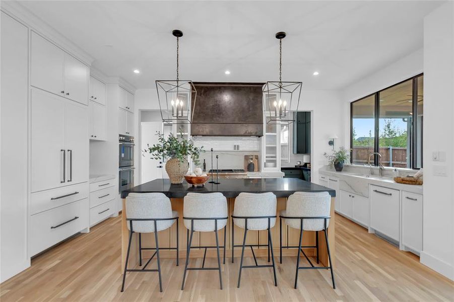 Kitchen with hanging lights, light wood finished floors, an island with sink, and dual tone cabinetry Kitchen with hanging lights, light wood finished floors, an island with sink, and dual tone cabinetry