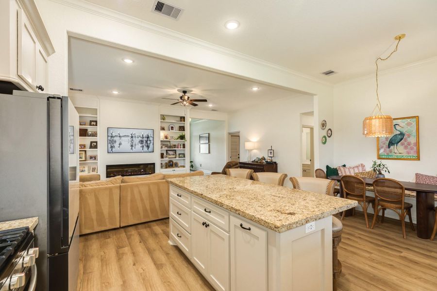 This inviting open-concept space features a modern kitchen with a large granite island, seamlessly flowing into a cozy living area with a fireplace and built-in shelves. Adjacent is a bright dining area with stylish lighting, perfect for entertaining.
