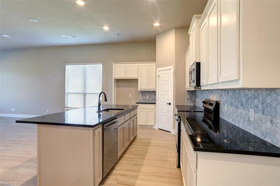 Kitchen with stainless steel appliances, backsplash, dark stone countertops, white cabinetry, and recessed lighting Kitchen with stainless steel appliances, backsplash, dark stone countertops, white cabinetry, and recessed lighting