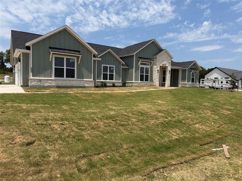 Contemporary ranch-style residence featuring a board and batten facade in a muted green, white trim accents, and a stone wainscoting
