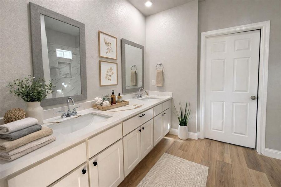 Full bathroom featuring double vanity, light wood-style floors, and a textured wall Full bathroom featuring double vanity, light wood-style floors, and a textured wall