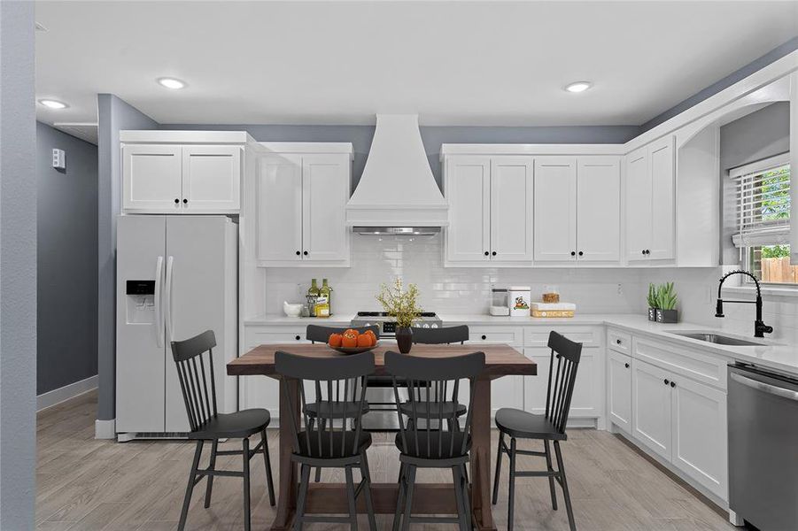 Kitchen featuring stainless steel appliances, backsplash, white cabinetry, custom range hood, and light wood-style floors Kitchen featuring stainless steel appliances, backsplash, white cabinetry, custom range hood, and light wood-style floors