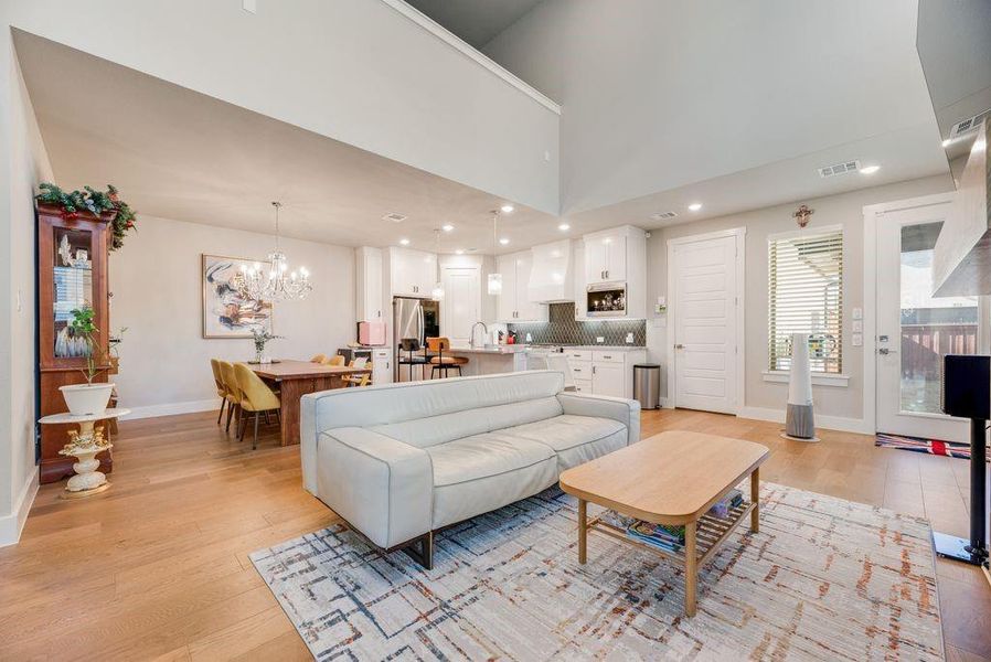 Living room featuring light wood-type flooring, a high ceiling, and a chandelier