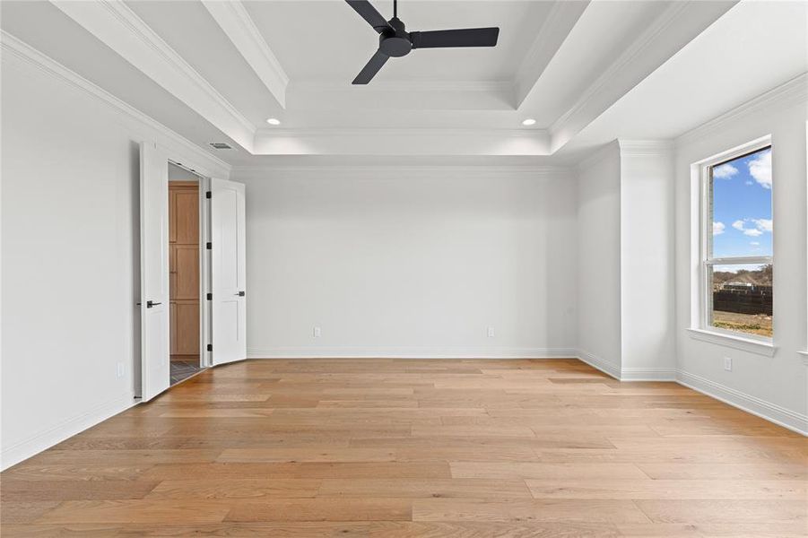 Empty room with ceiling fan, light wood-style floors, crown molding, recessed lighting, and a raised ceiling
