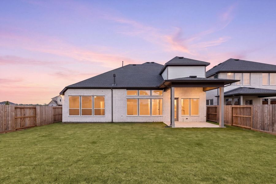 As evening falls, the backyard's covered patio and glowing windows create an inviting scene, framed by a fully fenced yard for privacy. As evening falls, the backyard's covered patio and glowing windows create an inviting scene, framed by a fully fenced yard for privacy.