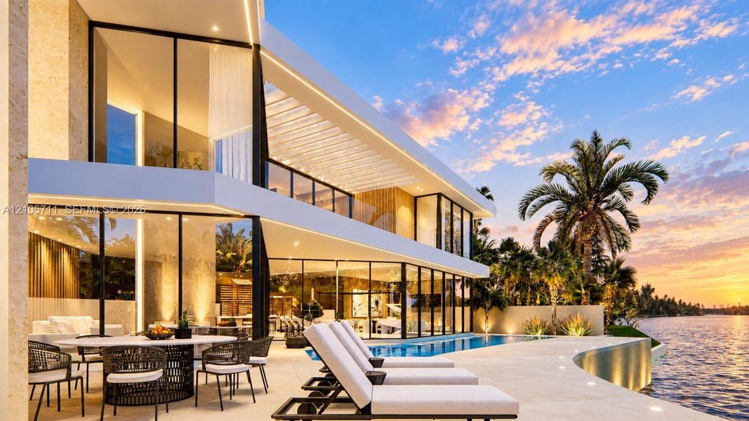 Modern waterfront estate featuring floor-to-ceiling glass walls, a covered stone patio, an infinity-edge swimming pool, and an expansive balcony with glass railings