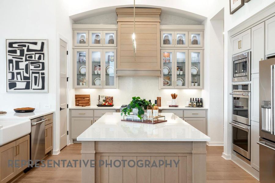 Kitchen featuring arched walkways, decorative light fixtures, appliances with stainless steel finishes, and light wood-style floors