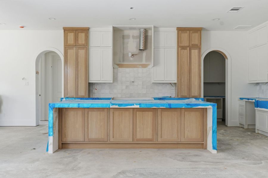 Straight on view of the kitchen as it comes together: custom cabinetry, a statement range wall, and an expansive island designed for storage, prep, and gathering. Finishes include a 4x4 backsplash, quartz countertops, and a full Thermador appliance suite.