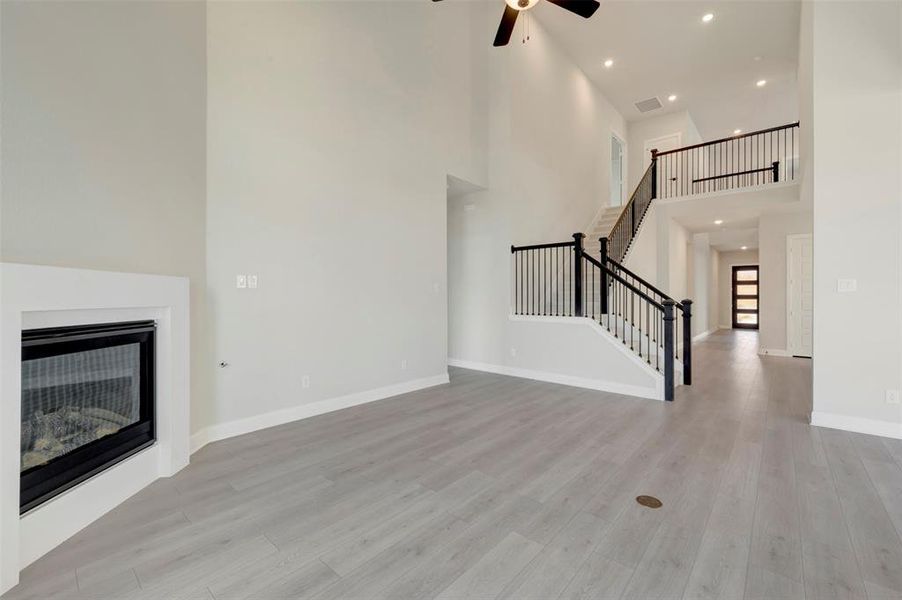 Unfurnished living room with a glass covered fireplace, ceiling fan, a high ceiling, light wood-type flooring, and recessed lighting