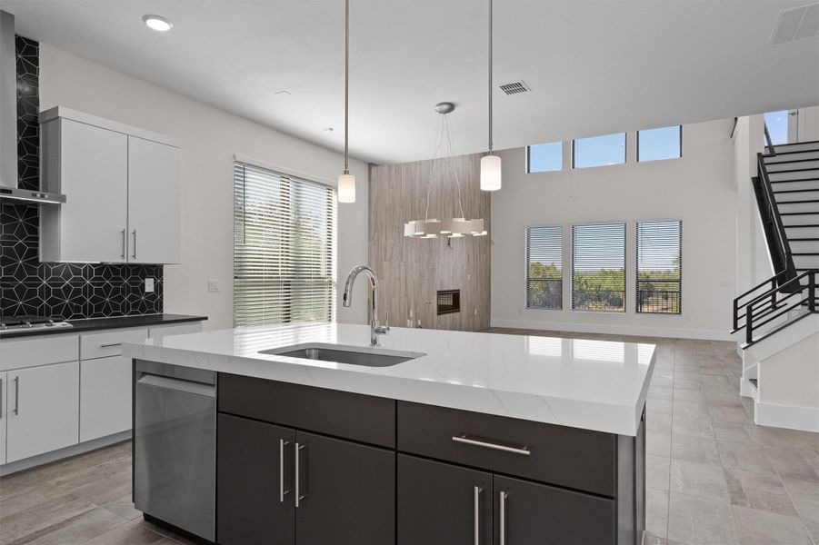 Kitchen with white cabinets, decorative light fixtures, dishwasher, an island with sink, and wall chimney exhaust hood Kitchen with white cabinets, decorative light fixtures, dishwasher, an island with sink, and wall chimney exhaust hood