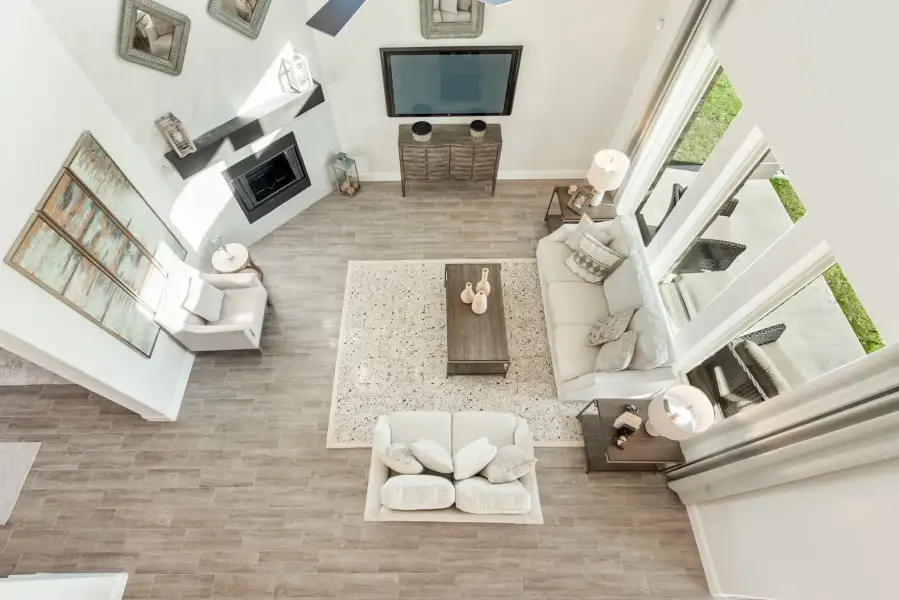 Overhead view of living room with white sofas, fireplace, wall-mounted TV, and wood-look tile floors