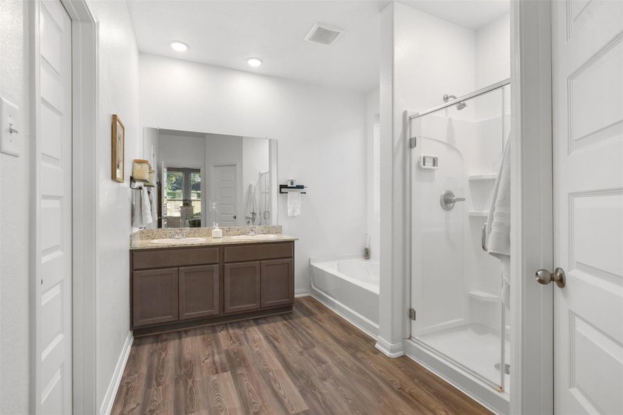 This inviting primary bath features a sleek glass shower, a relaxing tub, and a spacious dual-sink vanity, all enhanced by elegant wood cabinetry.