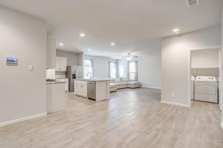 Kitchen featuring open floor plan, white cabinetry, a kitchen island with sink, independent washer and dryer, and light wood finished floors