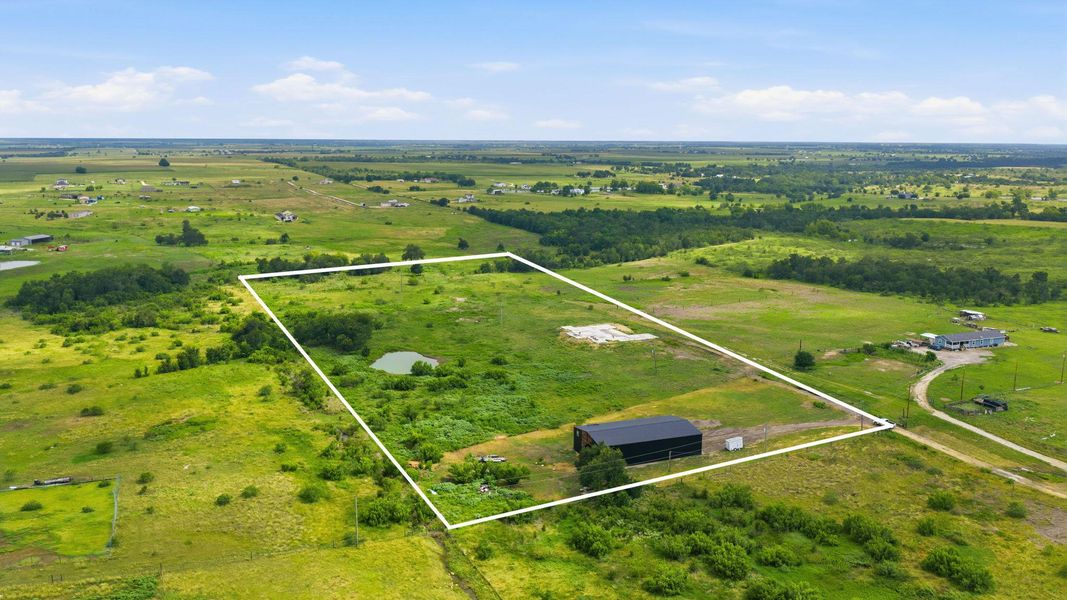 A vast expanse of green acreage with a clear pond, offering serene rural living.