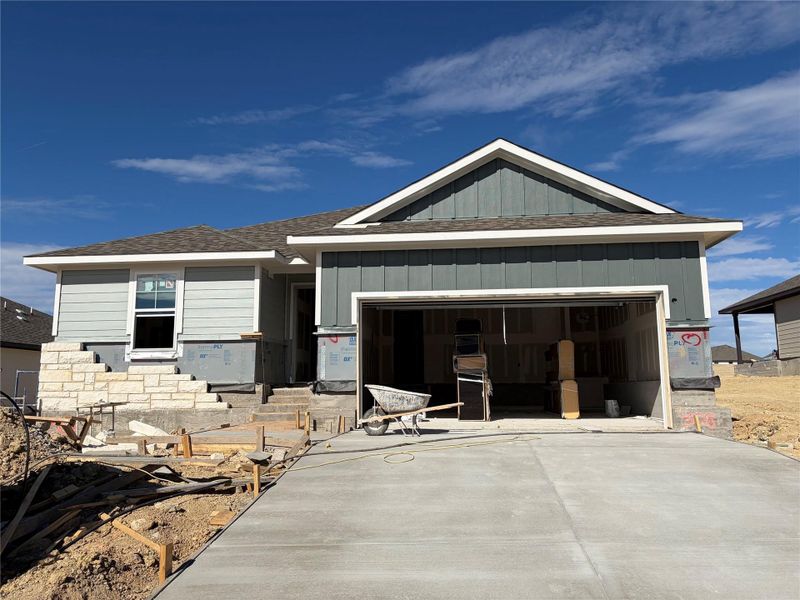 View of front of property featuring a shingled roof, an attached garage, board and batten siding, and driveway