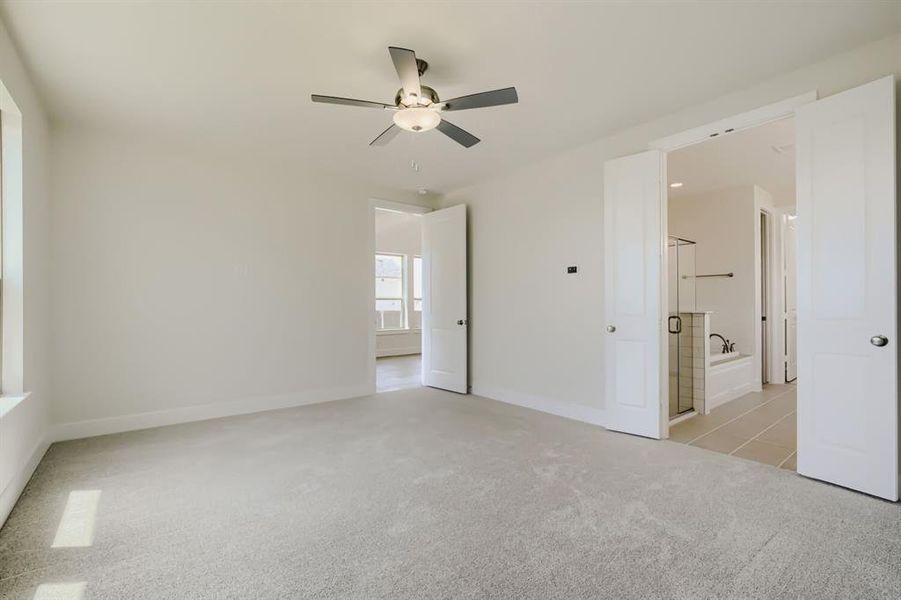 Carpeted room featuring a ceiling fan with integrated lighting, a window, and two paneled doors opening to a bathroom with a glass-enclosed shower and a bathtub
