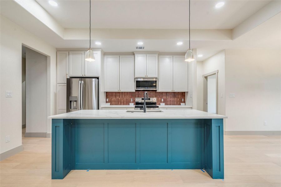 Kitchen featuring stainless steel appliances, white cabinetry, a raised ceiling, a center island with sink, and recessed lighting