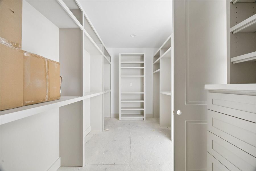 Generously sized walk in closet with custom built shelving and hanging space designed for maximum organization and functionality. Thoughtfully laid out to accommodate a full wardrobe, this space offers a combination of open shelving, long and short hanging areas, and dedicated storage for accessories. Clean lines and a bright, neutral palette create a boutique style feel within the primary suite.