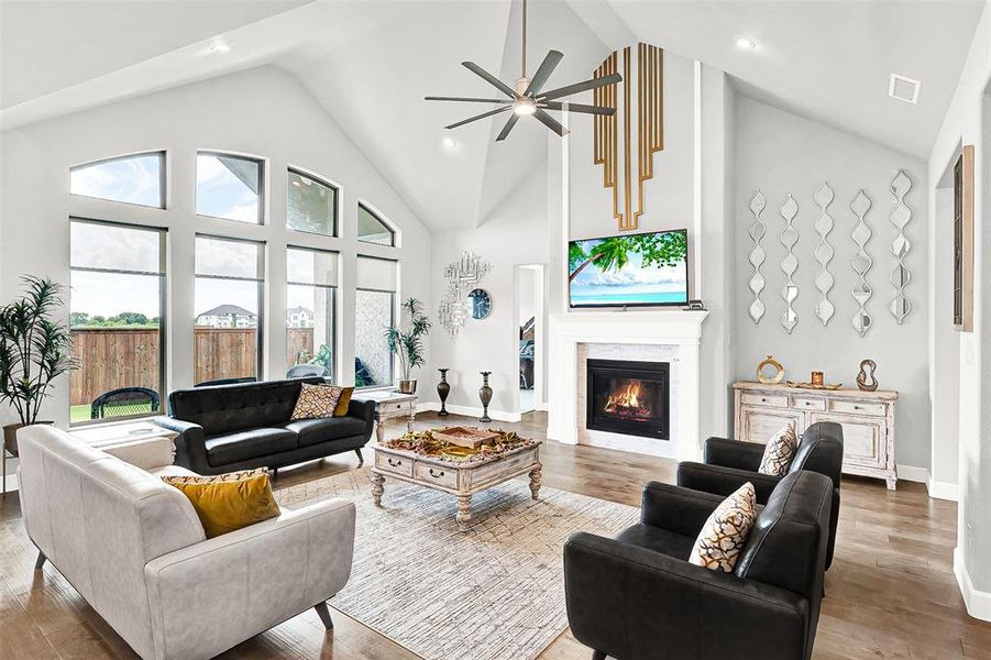 Living area with high vaulted ceiling, a glass covered fireplace, a ceiling fan, wood finished floors, and recessed lighting