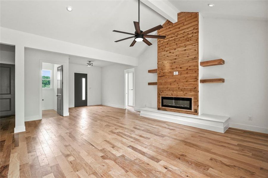 Unfurnished living room with a ceiling fan, light wood-style floors, a fireplace, beamed ceiling, and high vaulted ceiling